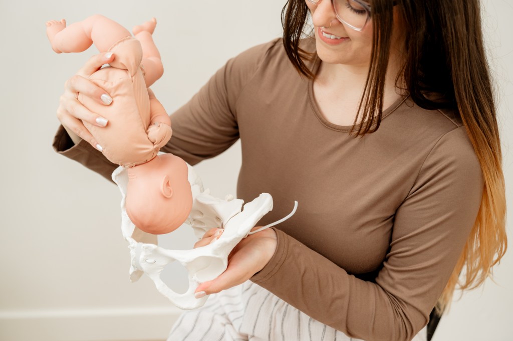 Doula holding baby prop at top of pelvis to simulate baby's descent in labor.